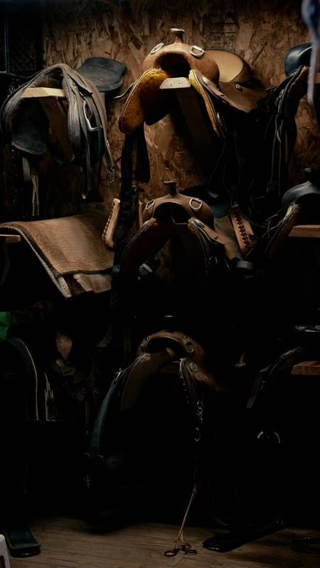 Horse riding saddles in a dark stable, reflecting preparation, trust and confident direction Horse riding saddles in a dark stable, reflecting preparation, trust and confident direction