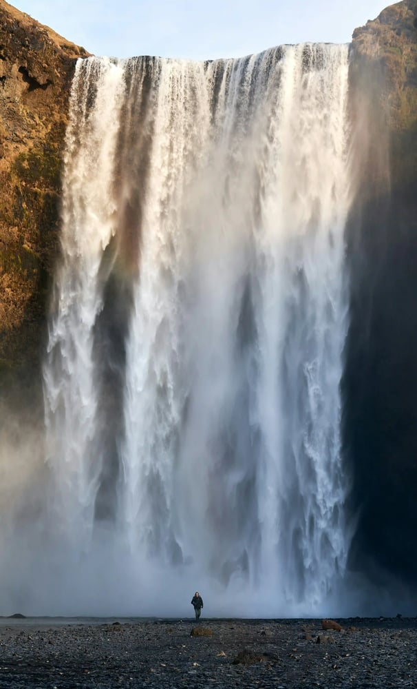 Lone walker at the foot of a huge waterfall, reflecting perspective, clarity and calm guidance