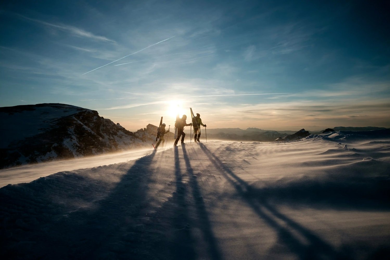 Skiers and snowboarder walking across a snowy ridge at sunset, reflecting resilience, preparation and shared purpose